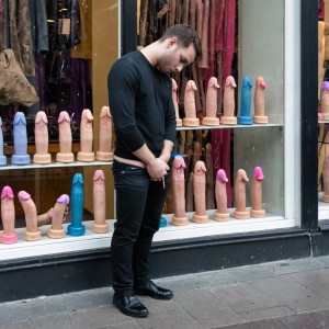 Un hombre sumiso muy triste mirando un escaparate lleno de dildos 